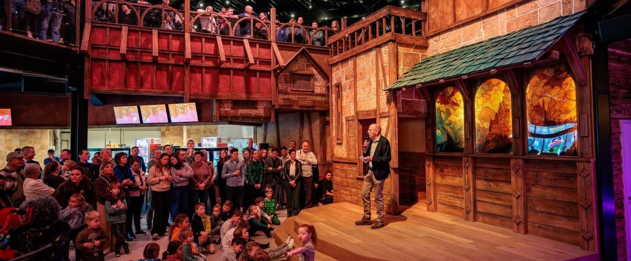 Ton Derks houdt een toespraak voor een groep kinderen en volwassenen in een middeleeuws decor voor de opening van de nieuwe binnenspeeltuin