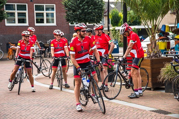 Group of cyclists in red sportswear stand ready with their bikes on a square in the centre of Nederweert.